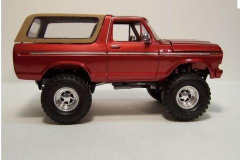 1978 Ford Bronco - A scale model of a red 1978-79 Ford Bronco shown in profile, featuring a tan removable hardtop, oversized off-road tires, chrome wheels, an…
