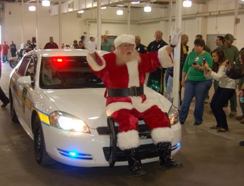 1991 Ford LTD Crown Victoria - Santa Claus poses on the hood of a white police car, which has its emergency lights activated.