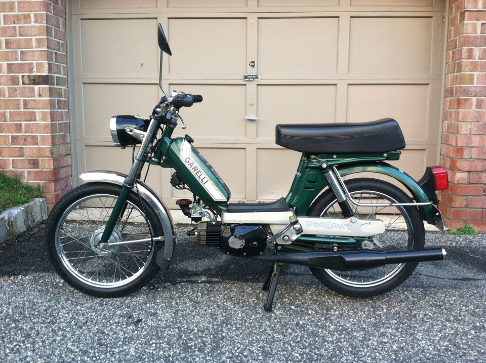 Green moped parked in front of a garage door. It has 'GARELLI' on the tank and 'SPORT' on the rear fender