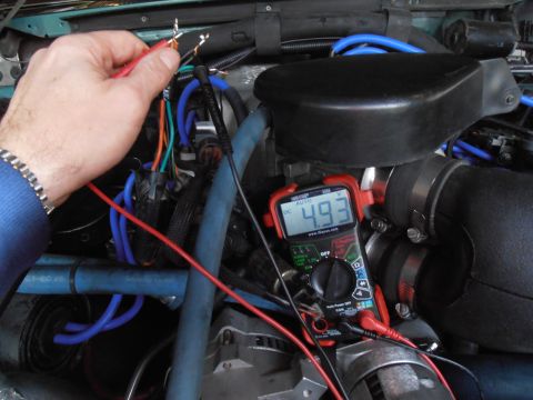 1990 Ford Bronco - A hand holds multimeter probes to wires in an engine bay, displaying a voltage reading.