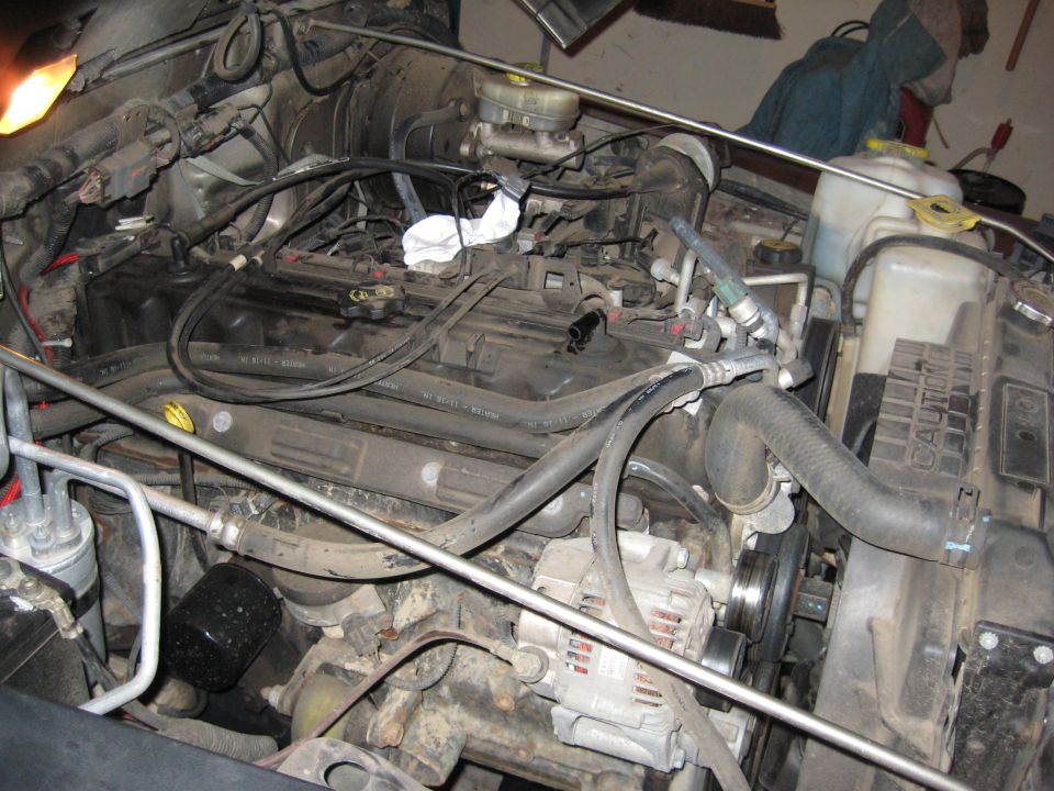 Engine bay of a 2005 Jeep Wrangler with visible alternator, hoses, and engine block