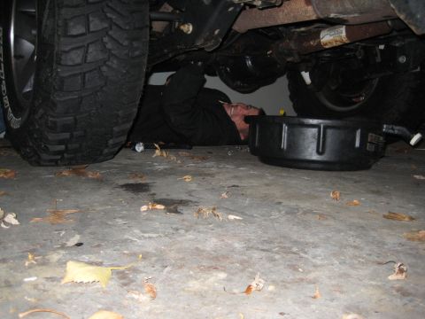 2005 Jeep Wrangler - A person works on the underside of a vehicle, with a large tire and an oil drain pan in view.