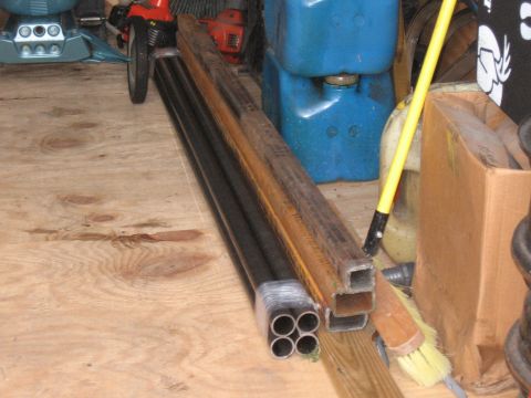 1994 Ford Bronco - A collection of metal pipes and lumber is stored on a plywood surface, with various containers and tools in the background.