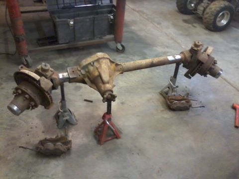 1995 Ford Bronco - Front axle assembly with disc brakes, supported by jack stands on a concrete floor.