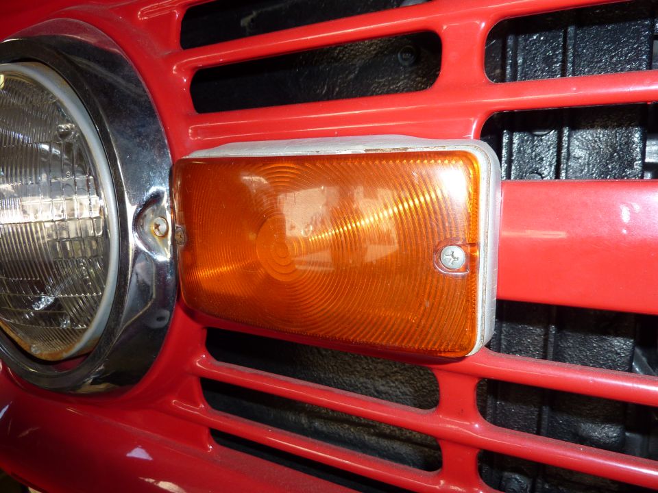 Close-up of an amber turn signal lens beside a round headlight on a red truck grille