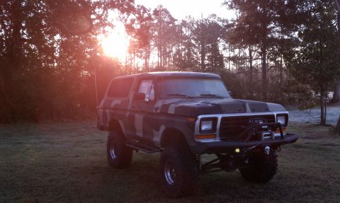 1979 Ford Bronco - This lifted Ford Bronco, painted in camouflage, sits in a field as the sun sets behind the trees.