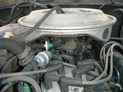 1979 Ford Bronco - Close-up view of a vehicle's engine bay, focusing on the carburetor and associated fuel lines and spark plug wires.