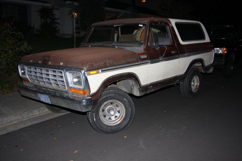 1979 Ford Bronco - This two-tone 1979 Ford Bronco shows significant rust on its hood and roof, parked curbside at night.