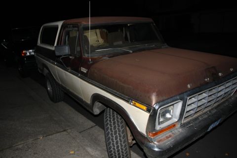 1979 Ford Bronco - This two-tone brown and white Ford Bronco is parked next to another vehicle at night.