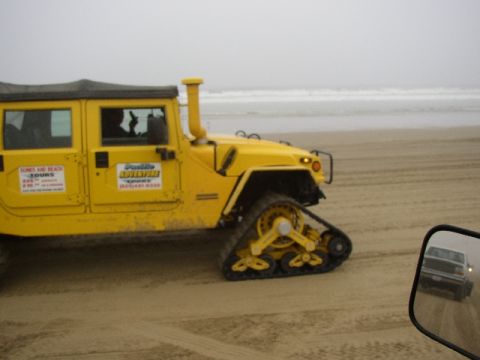 1989 Ford Bronco - A yellow tracked vehicle is on the beach, with another vehicle reflected in its side mirror.