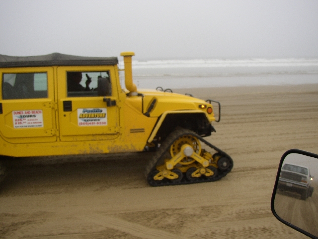 Yellow Hummer with rear track conversion on a foggy beach, tour signage on doors.