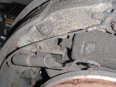 1979 Ford Bronco - Close-up view of a dusty and grimy brake drum and spring assembly, likely from an older vehicle.