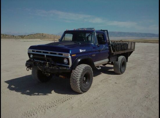 Blue Ford flatbed pickup with lift kit and off-road tires parked in desert