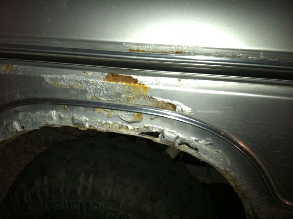 Severe rust and corrosion along the rear wheel arch and rocker of a silver truck at night