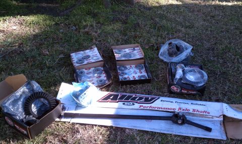 1979 Ford Bronco - Various differential components and performance axle shafts are displayed on the ground, suggesting a vehicle repair or upgrade.