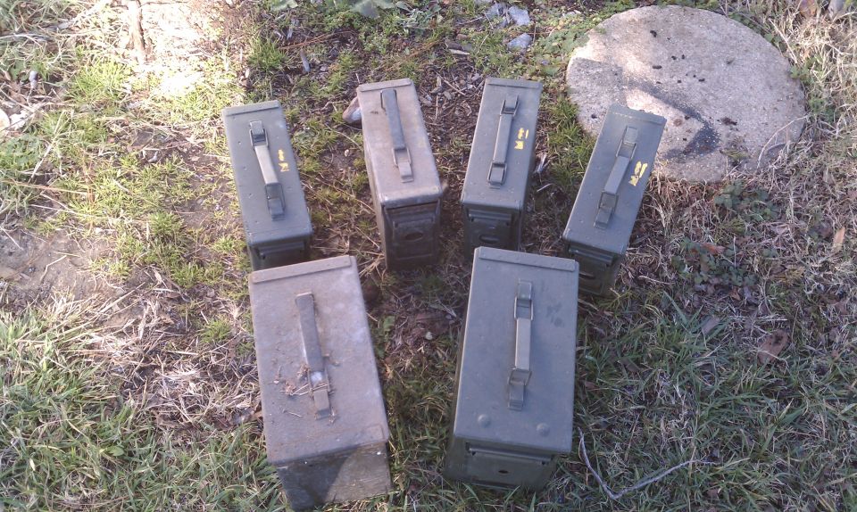 Several green ammo cans are scattered on the ground with grass and a rock