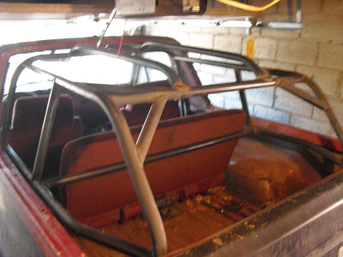 1986 Ford Bronco - The interior of a red Ford Bronco shows an aftermarket roll cage and orange seats.