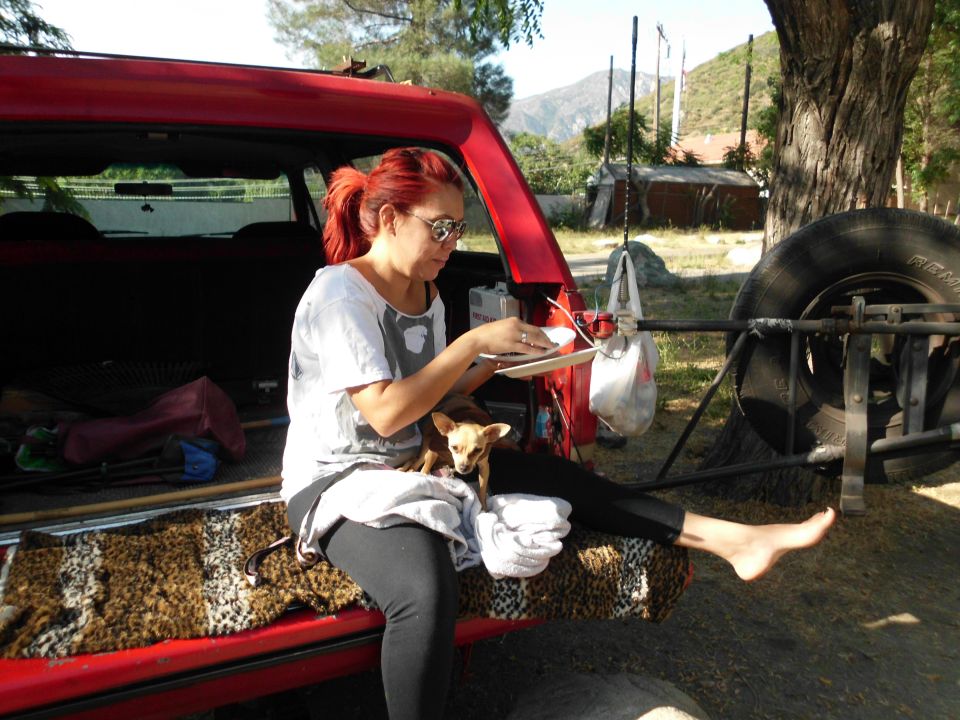 Woman with red hair and a small dog sitting in the open tailgate of a red SUV, with a spare tire mounted on the back