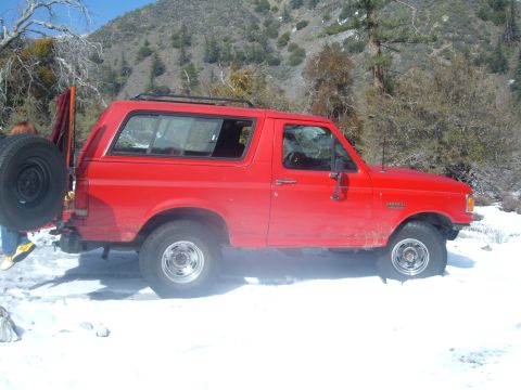 1988 Ford Bronco - A red 1988 Ford Bronco sits in a snowy, wooded area with mountains in the background.
