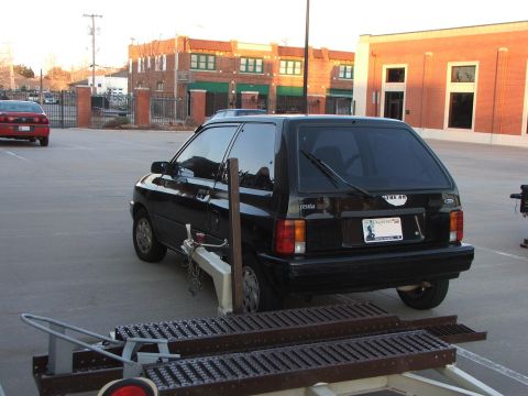 1991 Ford Festiva - Rear view of a black 1991 Ford Festiva, with a trailer hitch attached, and another car visible in the distance.