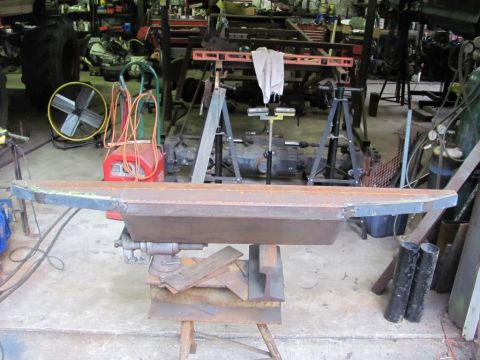 1982 Ford F-100 - A custom metal part is held in a vise in a workshop setting, with various tools and machinery visible.