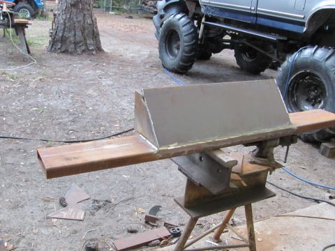 1982 Ford F-100 - A metal fabrication project is clamped in a vise, with a large tire and part of a truck visible in the background.