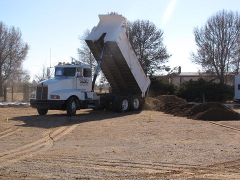 1995 Ford Bronco - A white dump truck is actively unloading a pile of dirt at a construction site on a clear day.