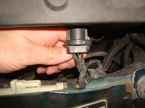 1995 Ford Bronco - A hand disconnects a headlight bulb connector, revealing the wiring harness.