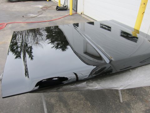 1987 Dodge 1500 - A freshly painted black car hood is shown resting on sawhorses outdoors.
