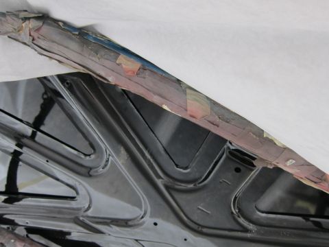 1987 Dodge 1500 - The underside of a car hood, covered in black paint, with a taped edge visible at the top.