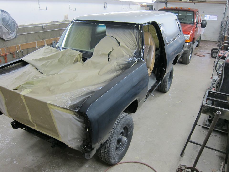 Black and silver SUV in a garage, covered in masking paper and plastic, with its doors open