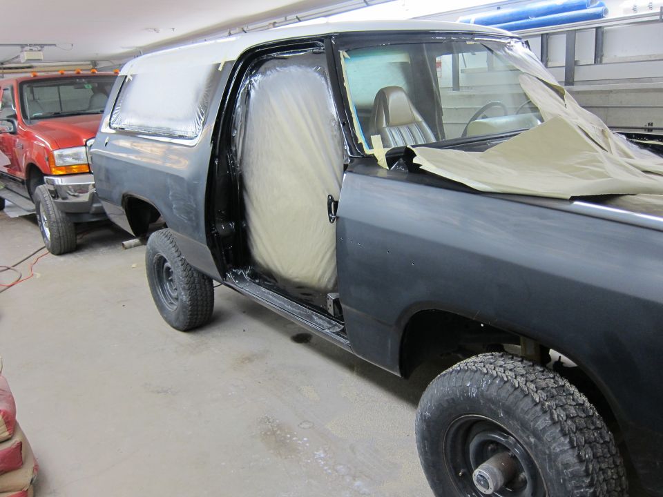 Dark gray SUV with doors open and covered in masking, parked next to a red truck