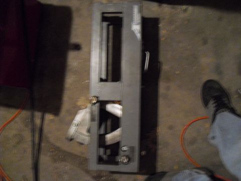 1986 Ford Bronco - A gray metal part with openings and a handle is shown on a concrete floor.