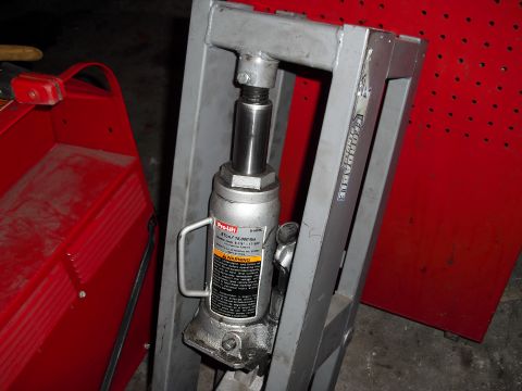 1986 Ford Bronco - A hydraulic press and bottle jack are shown in a workshop setting, with a red toolbox nearby.