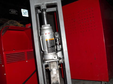 1986 Ford Bronco - A hydraulic bottle jack is shown mounted in a metal frame, with a red tool chest visible behind it.