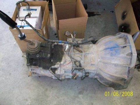 2000 Isuzu Vehicross - Transmission assembly with shifter and electrical connectors, resting on a concrete floor.