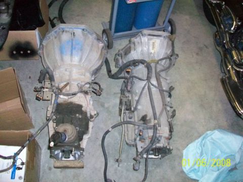 2000 Isuzu Vehicross - Two vehicle transmissions are shown side-by-side on a concrete floor, each with attached wiring.
