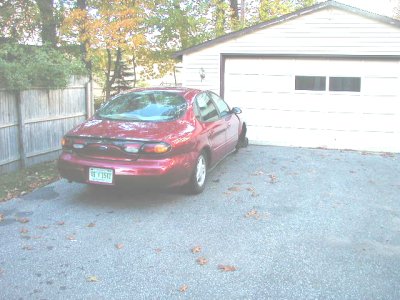 1997 Ford Taurus - A red 1997 Ford Taurus is parked in a driveway next to a garage.