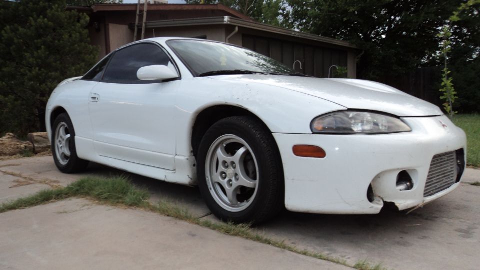 White 1998 Mitsubishi Eclipse coupe with damaged front bumper and aftermarket wheels parked on a driveway