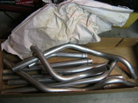 1979 Ford Bronco - A collection of bent exhaust pipes are piled inside a cardboard box, partially covered by paper.