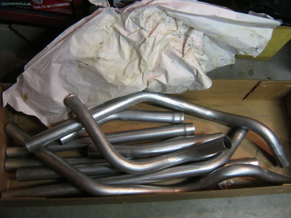 Box of bent metal exhaust pipes, some covered in crumpled paper