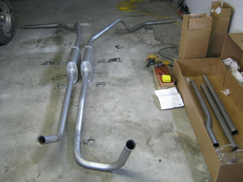Exhaust pipes and mufflers laid out on a concrete floor with boxes and tools