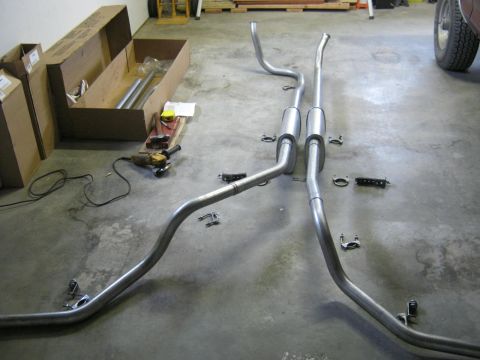 1979 Ford Bronco - New exhaust system components are laid out on a concrete floor, ready for installation.