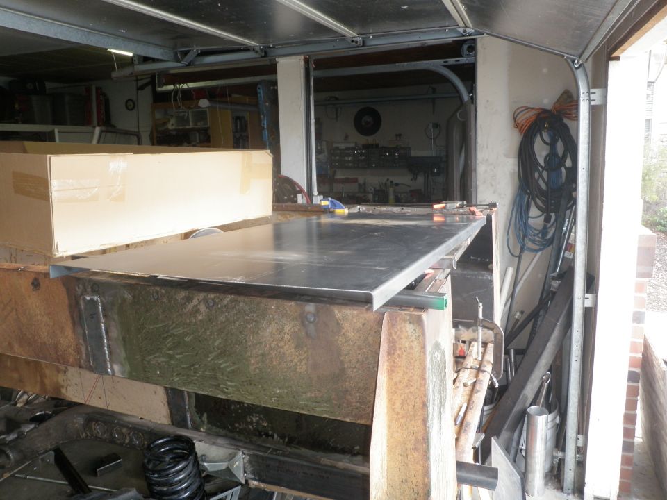 Metal sheet resting on a rusty metal frame in a garage workshop. A cardboard box is on the left