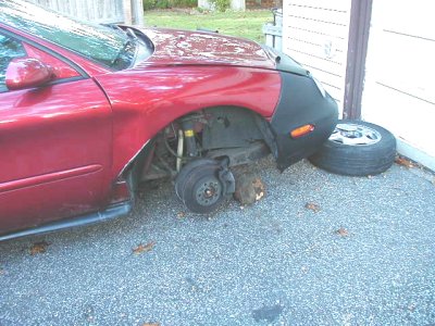 1997 Ford Taurus - This red sedan is missing its front passenger wheel and is propped up on blocks. A spare tire rests against the wall.
