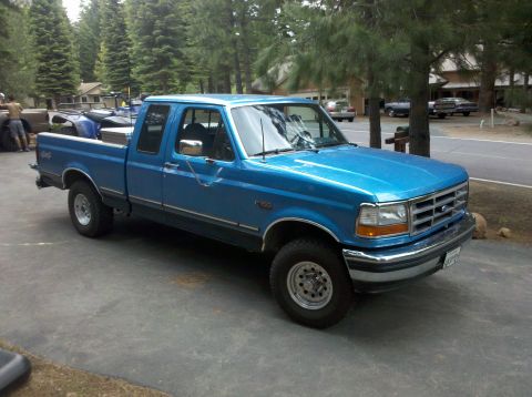 1992 Ford F-150 - This blue 1992 Ford F-150 pickup truck is parked outside a residence with trees in the background.