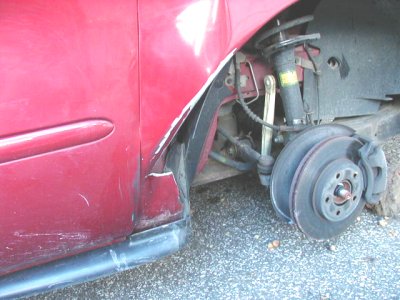 1997 Ford Taurus - Close-up of a damaged red car fender and wheel assembly, revealing suspension parts.