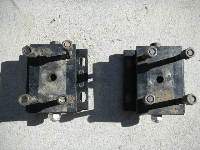 Two black engine mounts with bolts and nuts on a concrete surface