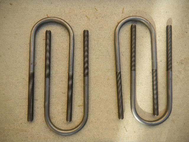 Two u-bolts, one larger than the other, lying on a concrete surface