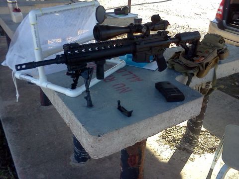 1996 Ford Bronco - A rifle with a scope and bipod is set up on a table, with a cell phone and tactical gear nearby.
